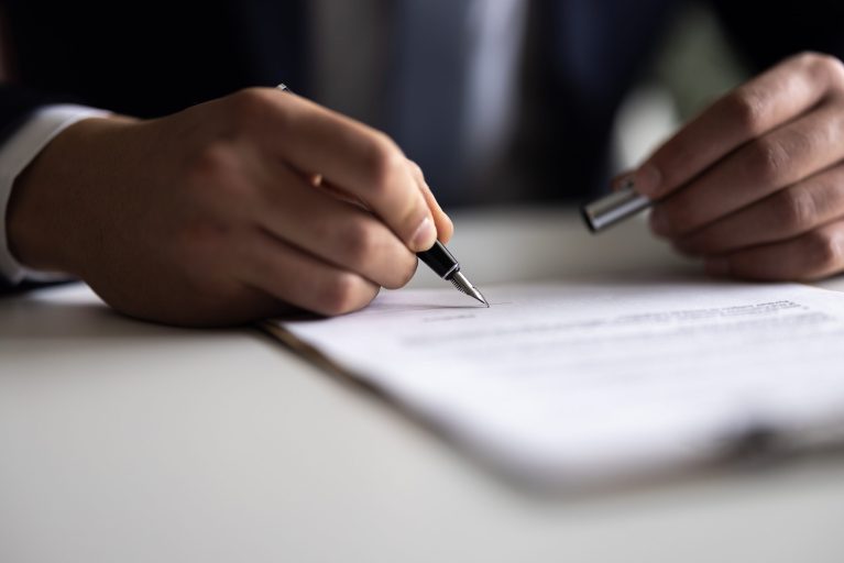 Person signing a document with a pen
